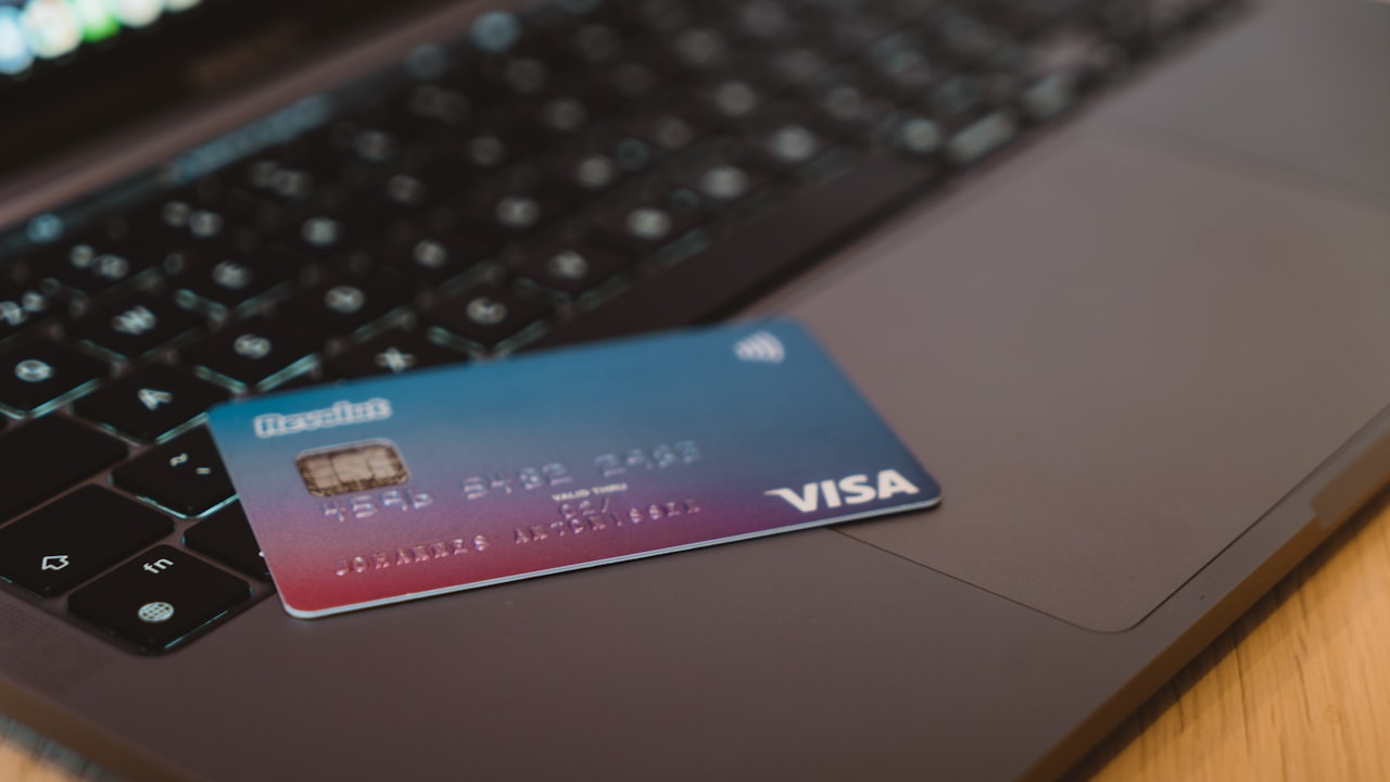 A blue and red gradient debit card resting on a dark laptop keyboard
