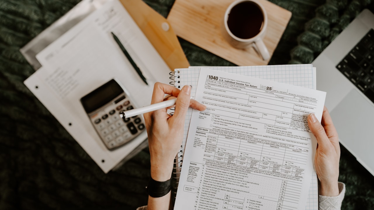 Person reviewing documents with calculator and laptop.